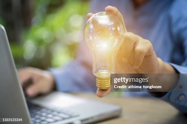 hand of businessman holding illuminated light bulb, idea, innovation and inspiration concept. - man blue background fotografías e imágenes de stock