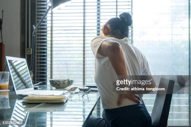 woman holding her back pain while working on computer at home. - rückenschmerzen stock-fotos und bilder