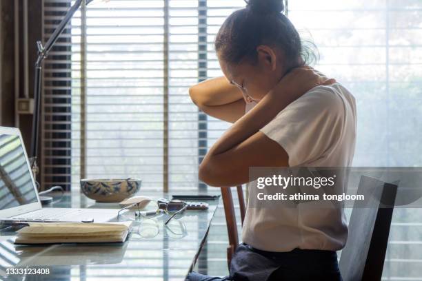 woman holding her neck in pain while working on computer at home. - menselijke nek stockfoto's en -beelden