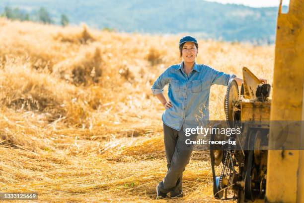 portrait of young female farmer with combine harvester machine in farm field - combine harvester stock pictures, royalty-free photos & images