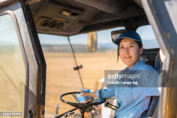 portrait of young female farmer sitting in combine harvester machine and smiling for camera - agricultural equipment stockfoto's en -beelden