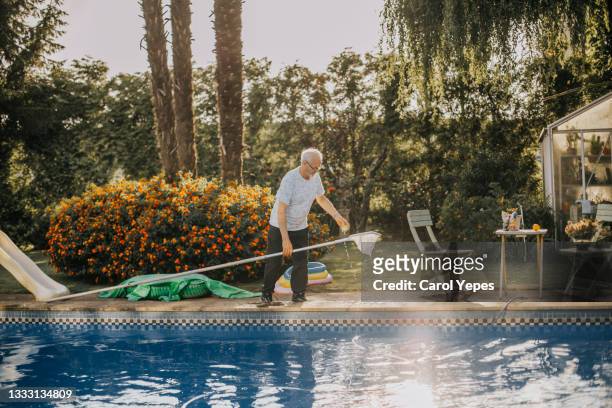 senior man keeping clean the pool with fishing net - swimming pool cleaning stock pictures, royalty-free photos & images