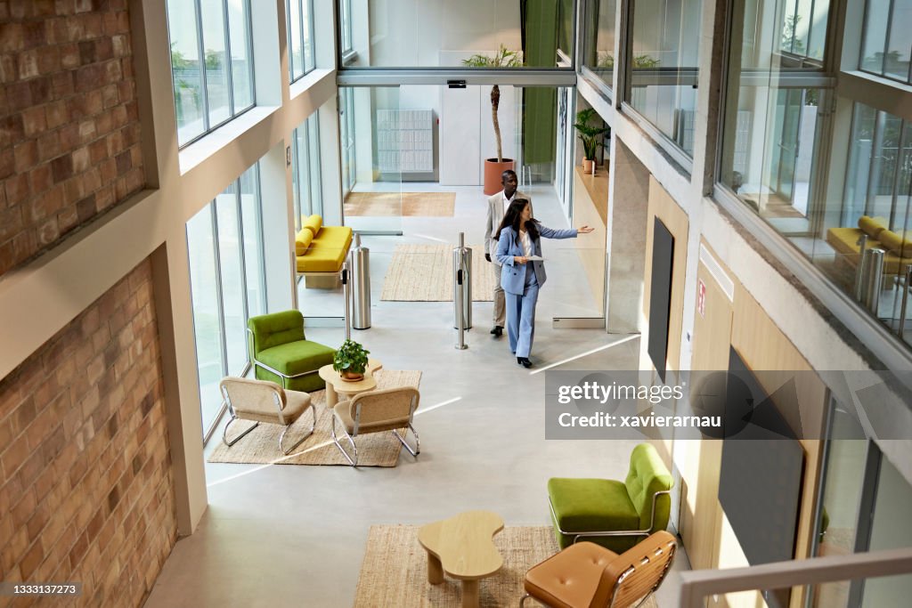 Real Estate Agent Leading Client Through Modern Office Building Lobby