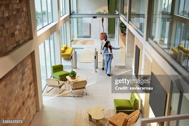 real estate agent leading client through modern office building lobby - commercial real estate agent stock pictures, royalty-free photos & images