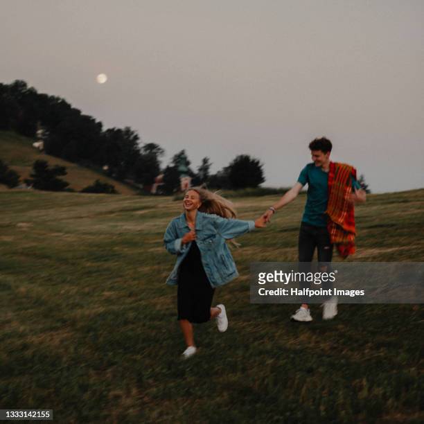 portrait of young couple on a walk outdoors in nature, running at sunset. - young couple enjoying a walk through grassland stock pictures, royalty-free photos & images