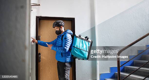 man indoors by front door in block of flats, food delivery and coronavirus concept. - delivery boy stock-fotos und bilder