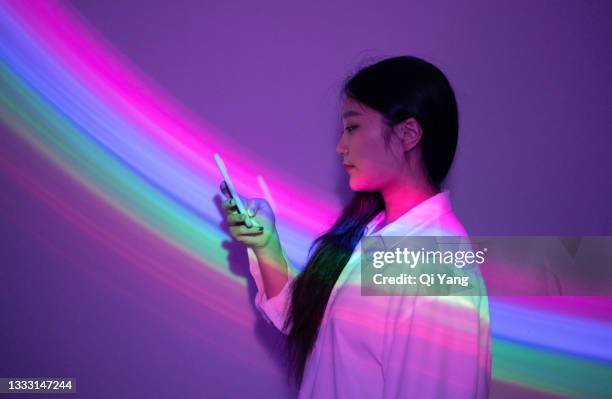 young asian woman using smartphone on rainbow background - augmented reality phone stock-fotos und bilder