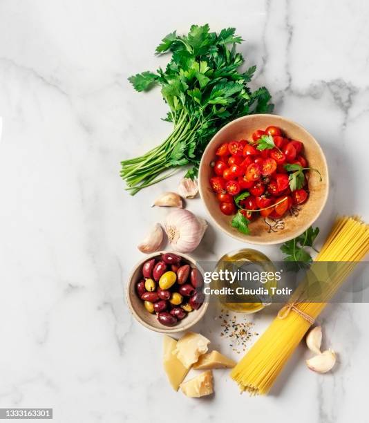 food ingredients (tomatoes, parsley, olives, garlic, parmesan, olive oil, and spaghetti) on white background - ingrédients photos et images de collection