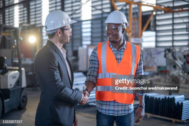 friendly factory engineers join hands in the mechanical factory control room. - black men shaking stock pictures, royalty-free photos & images