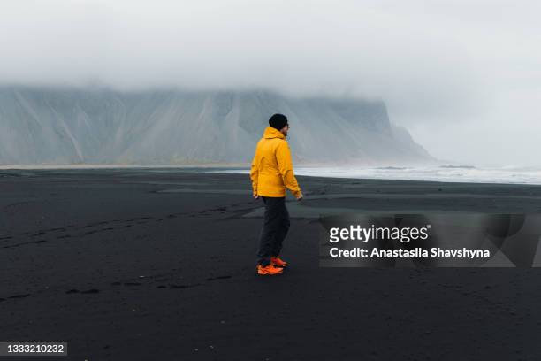 young man traveler exploring the moody black sand beach with mountains view - black sand iceland stock pictures, royalty-free photos & images