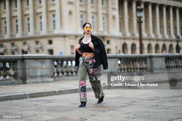 Lycia Lamini wears orange with pearls sunglasses, black and white large Japanese character pendant earrings, silver and rhinestones chain necklace, a...