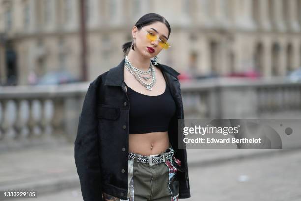 Lycia Lamini wears orange with pearls sunglasses, black and white large Japanese character pendant earrings, silver and rhinestones chain necklace, a...