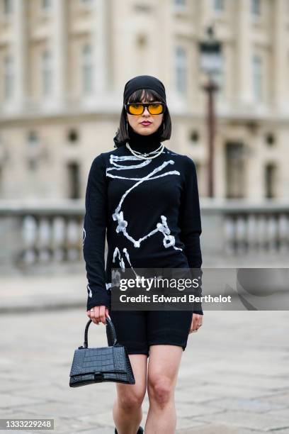 Hélène Guillaumes wears a black scarf from Louis Vuitton as a beanie, black and orange sunglasses, silver large earrings, white pearls necklaces, a...