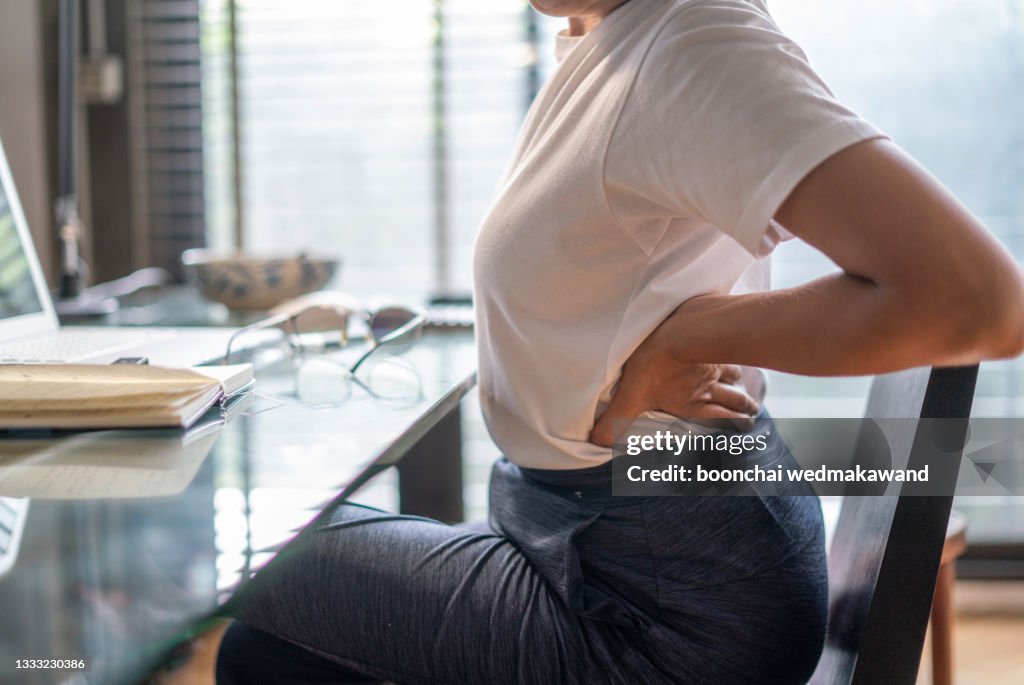 Woman in home office suffering from back pain sitting at computer desk