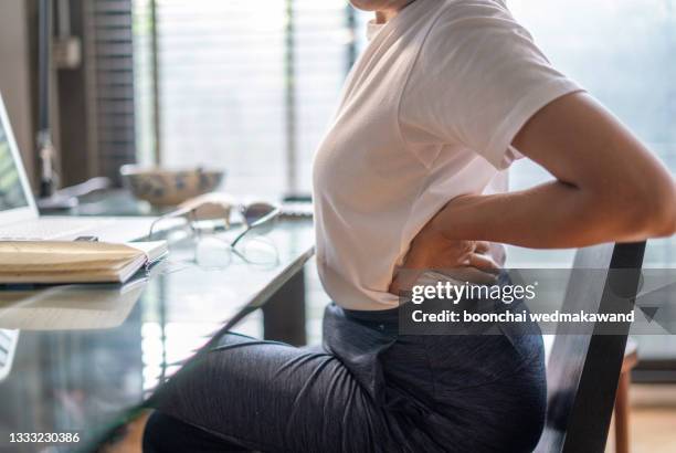 woman in home office suffering from back pain sitting at computer desk - sitting working stockfoto's en -beelden