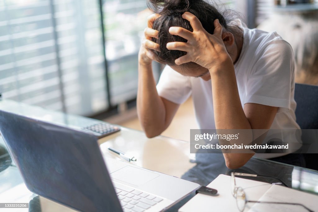Tired young business woman or student with a headache using laptop at the home office.