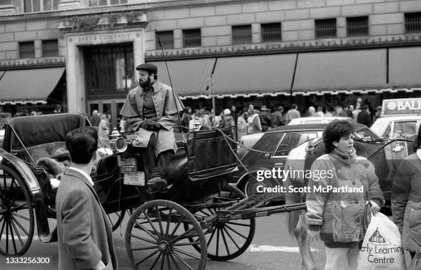 View of a coachman waiting in his horse-drawn carriage, parked across the street from Saks & Company on 5th Avenue , New York, New York, December 27,...