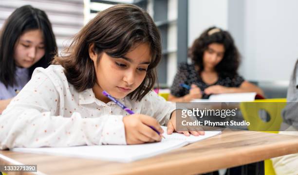 elementary school girl smiles at the camera as she sits at her desk in her classroom - 10 11 jaar stockfoto's en -beelden