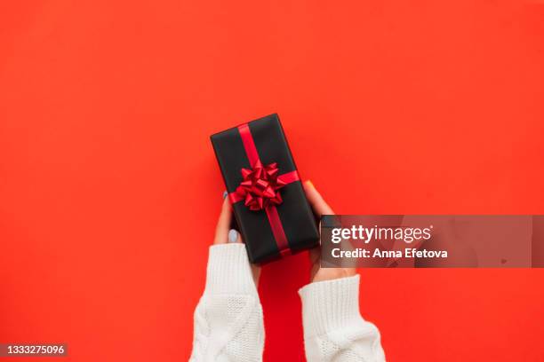 black gift box with red bow in woman hands on red background. black friday shopping concept. copy space for your design - hand white background stock pictures, royalty-free photos & images