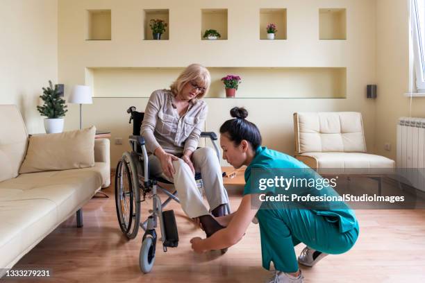 sick old woman in a wheelchair is receiving a help from a young nurse in home visit. - kinesist stockfoto's en -beelden