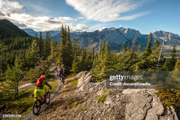 view of mountain bikers following trail down mountain - bicycle trail outdoor sports stock pictures, royalty-free photos & images