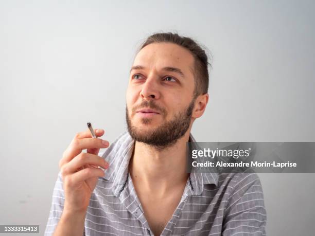 caucasian man in gray shirt smokes a cigarette in white room in medellin, colombia - human joint stock-fotos und bilder