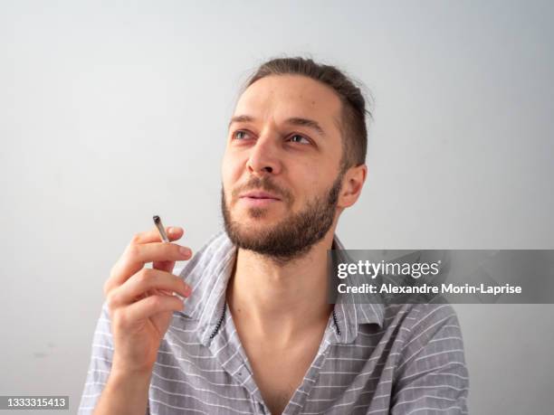 caucasian man in gray shirt smokes a cigarette in white room in medellin, colombia - roll shirt stock pictures, royalty-free photos & images