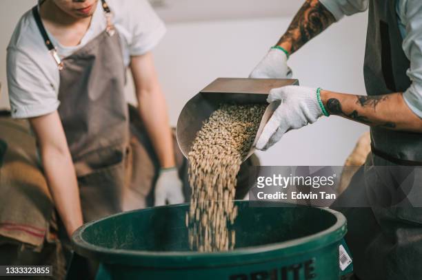 menschliche hand gießen rohe kaffeebohne auf lagereimer mit schaufel gewichten und mischen - same action stock-fotos und bilder