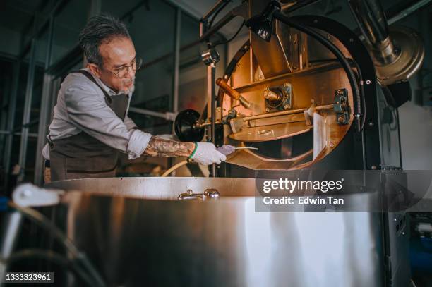 asian chinese working senior man with glove brushing and cleaning coffee roaster machine with vacuum cleaning - bier brouwen stockfoto's en -beelden