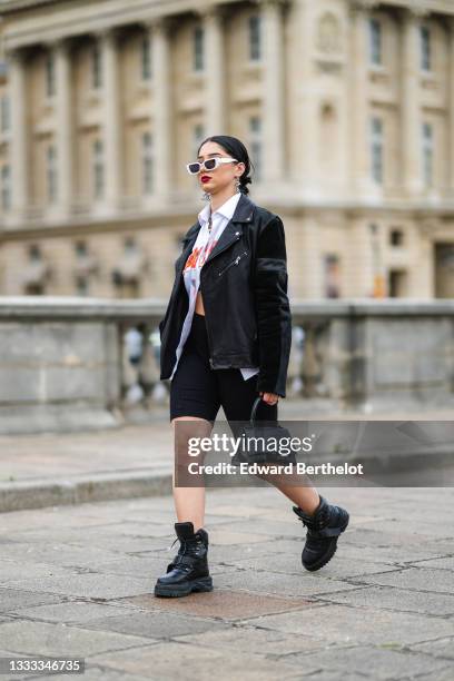 Lycia Lamini wears white sunglasses, black and white large Japanese character pendant earrings, a silver and rhinestones chain necklace, a silver...