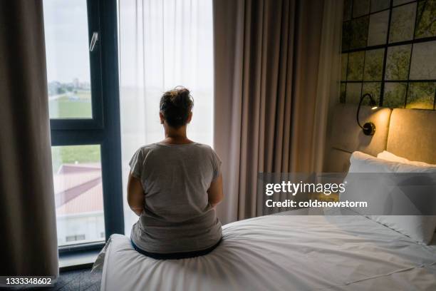 woman sitting alone on bed in hotel room - abuse imagens e fotografias de stock