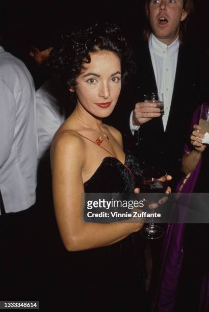 American singer, songwriter and guitarist Jane Wiedlin, wearing a black off-shoulder outfit, holding a wine glass at an unspecified event, location...