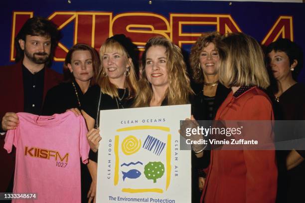An unspecified man holds a pink 'KIISFM 102.7' t-shirt, alongside members of American New Wave band The Go-Go's and American actress Jane Fonda at...