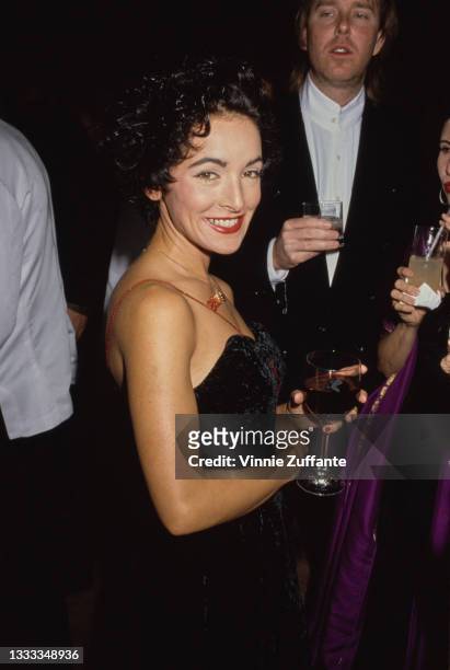 American singer, songwriter and guitarist Jane Wiedlin, wearing a black off-shoulder outfit, holding a wine glass at an unspecified event, location...