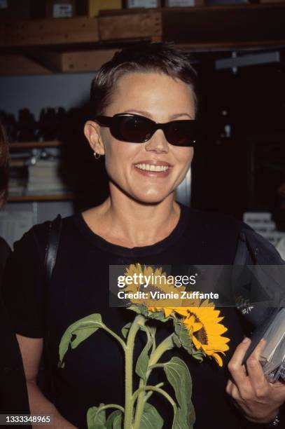 American singer and musician Belinda Carlisle wearing sunglasses and holding a sunflower as her band, American New Wave band The Go-Go's, held an...