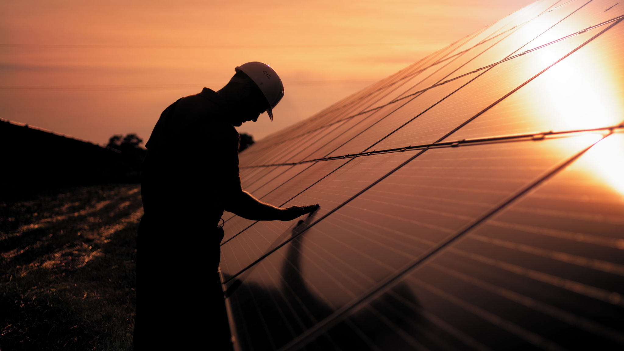 Assistance technical worker in uniform is checking an operation and efficiency performance of photovoltaic solar panels. Unidentified solar power engineer touches solar panels with his hand at sunset Assistance technical worker in uniform is checking an operation and efficiency performance of photovoltaic solar panels. Unidentified solar power engineer touches solar panels with his hand at sunset
