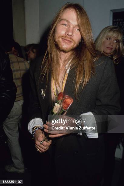 American singer, songwriter and musician Axl Rose, wearing a black suit jacket with the cuffs folded back, holding a small bunch of roses, event...