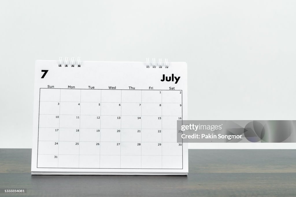 Calendar desk 2022 July month for organizer to plan and reminder on wooden table with white color old grunge wall concrete background.