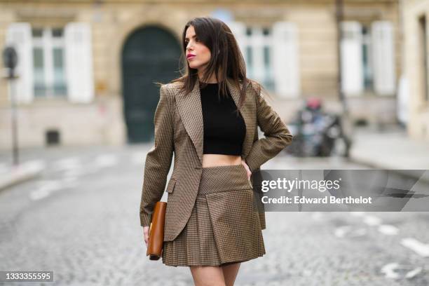 Sara Carnicella wears a black ribbed halter-neck cropped t-shirt, a black / beige / brown checkered print pattern long blazer jacket, a matching...