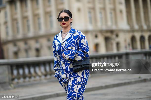 Lycia Lamini wears black and white large Japanese character pendant earrings, black sunglasses, a silver and rhinestones chain necklace, a silver...