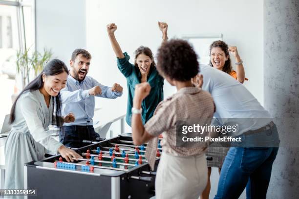 coworkers playing table football - fun at work stockfoto's en -beelden