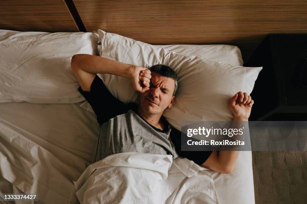 adult man waking up. stretching with her arms up on her bed. - man sleeping pillow stock-fotos und bilder