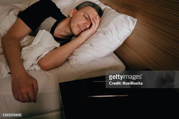 adult man in bed looking at cell phone alarm - can't sleep stock-fotos und bilder