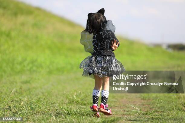 little girl in halloween costume black dress,wings and ear jumping outdor in back view - girls hands behind back stock-fotos und bilder