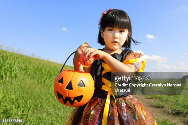 little girl in halloween costume with jack o lantern looing at camera - halloween ball stockfoto's en -beelden