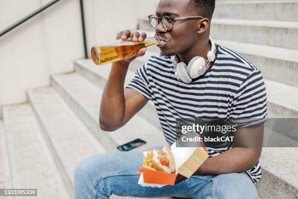 close up portrait of young man eating hot dog and drinking beer - over eating stock pictures, royalty-free photos & images