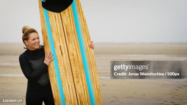 woman holding surfboard while standing at beach against sky,germany - jonas weinitschke stock pictures, royalty-free photos & images