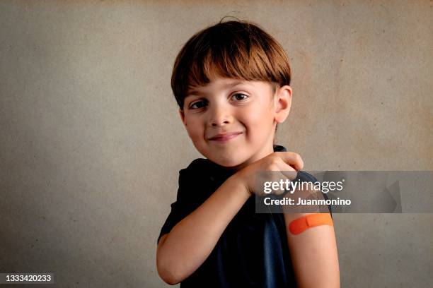 sorridente bambino di sei anni subito dopo essere stato vaccinato mostrando un aiuto al divieto sul braccio - 4 5 years foto e immagini stock