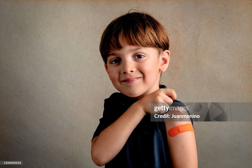 Smiling Six years old child just after being vaccinated showing a ban aid on his arm
