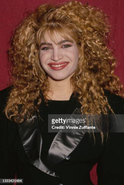 American singer, songwriter, and actress Taylor Dayne wearing a black jacket with black silk lapels poses in front of a red backdrop, circa 1990.